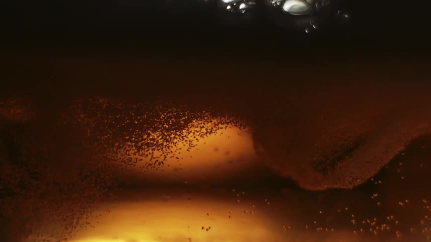 Closeup view of bubbles and foam in a goldenbrown liquid with light reflecting through it creating an amber glow