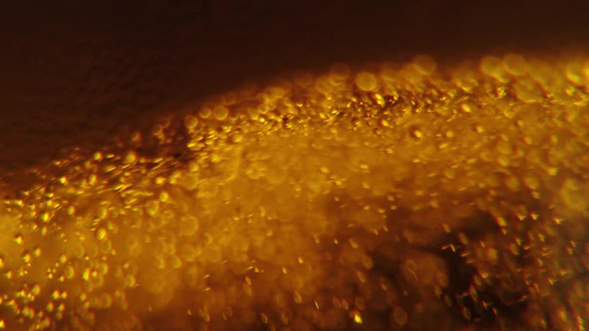 Closeup view of bubbles and foam in a goldenbrown liquid with light reflecting through it creating an amber glow