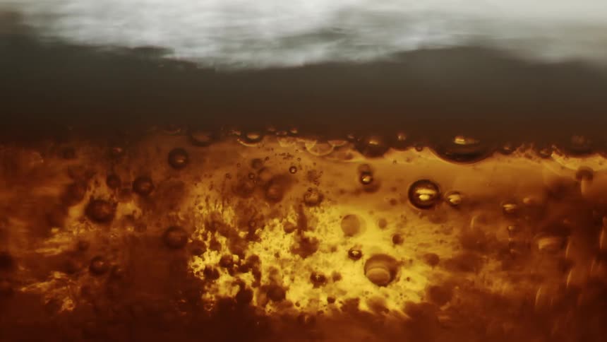 Closeup view of bubbles and foam in a goldenbrown liquid with light reflecting through it creating an amber glow