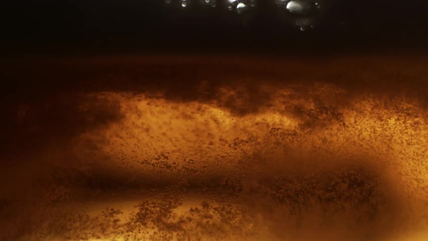 Small bubbles rise towards the larger bubbles floating on the surface of an alcoholic beverage