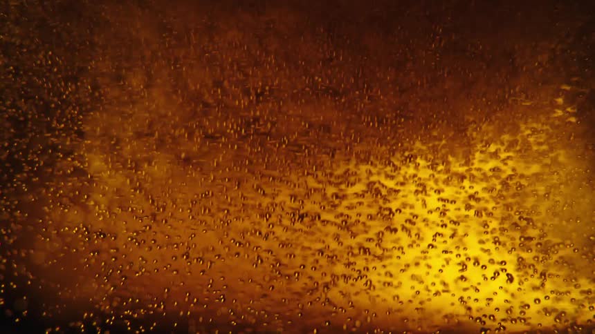 Closeup view of bubbles and foam in a goldenbrown liquid with light reflecting through it creating an amber glow