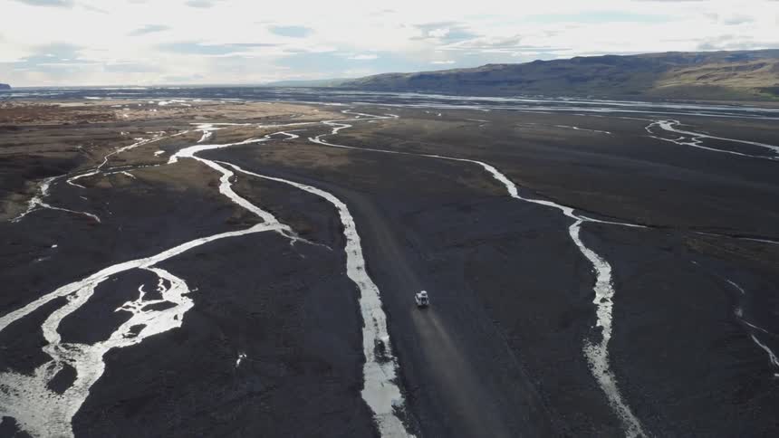 Aerial view  of a vehicle driving on a dirt road with small rivers to each side on a cloudy day