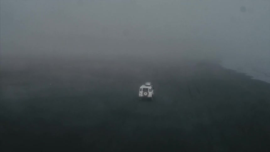 A vehicle driving on some land where there is a lot of smoke or fog and you cannot really see anything