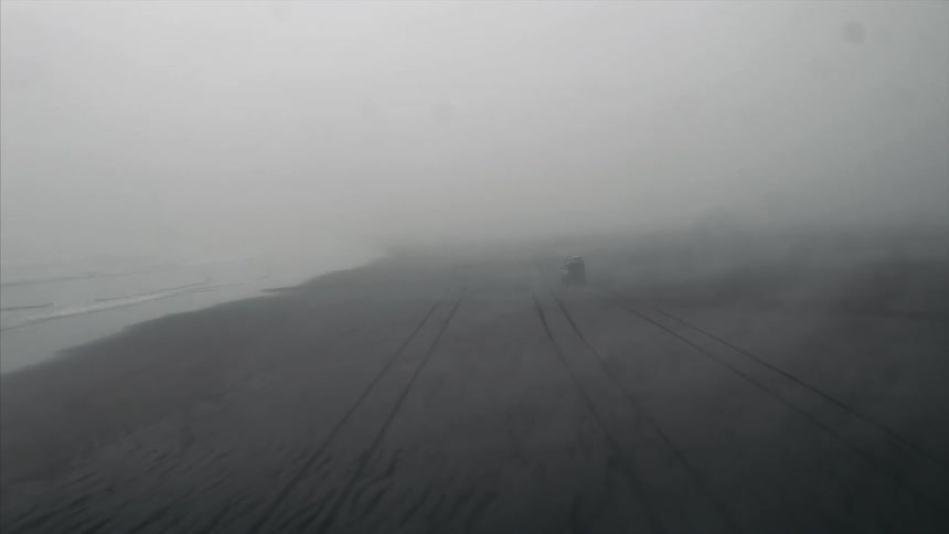 Vehicle driving  on a beach through heavy mist and clouds