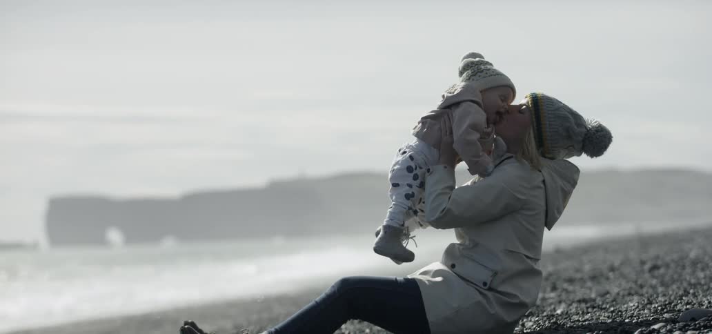 A woman is playfully lifting a young child on the beach