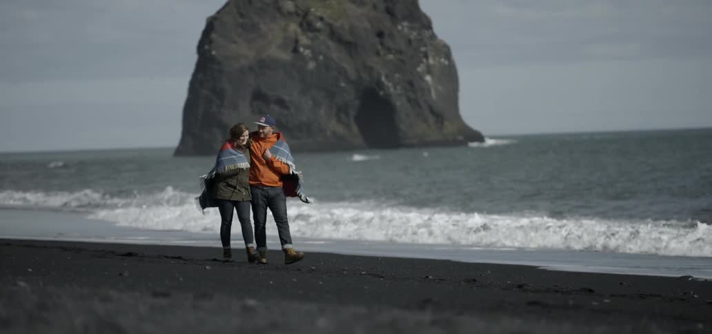 A man and woman walked down the beach wrapped in a blanket