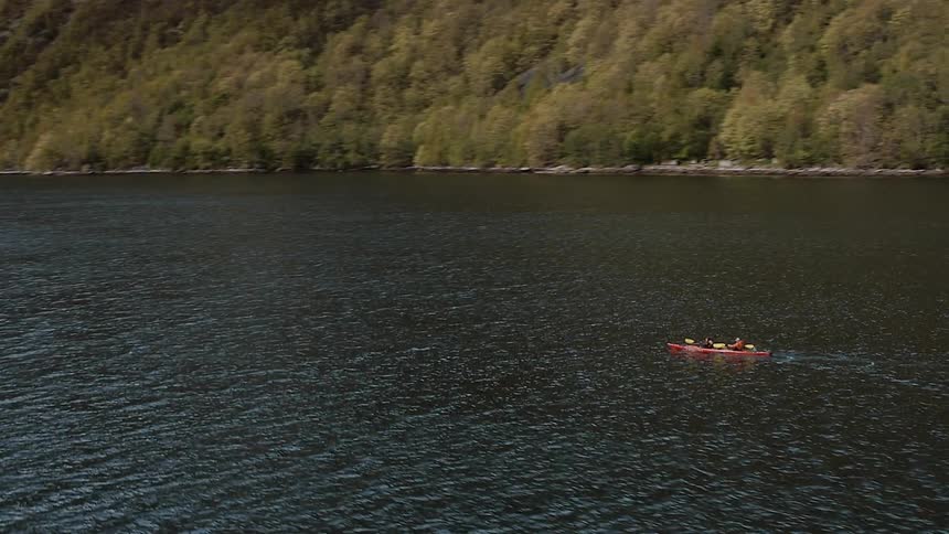 Two people rowing rhythmically in a red boat as seen from the air