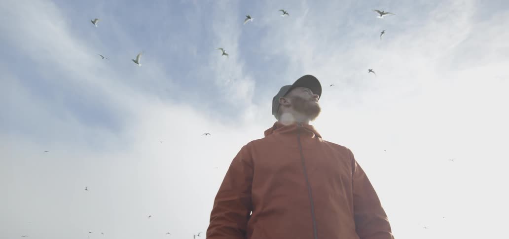 Bearded hiker looking up towards birds soaring above him on a cloudy day
