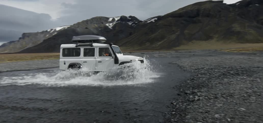 A white jeep is driving through a large area of water after coming off of dry land