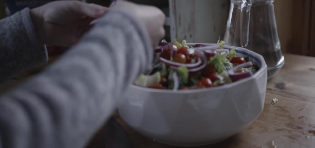 Woman  placing sliced onions onto a salad that she is making in a bowl