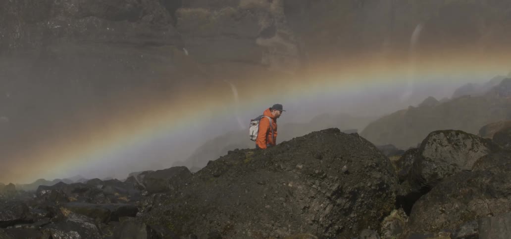 Hiker traversing a rocky area  with a rainbow in the background