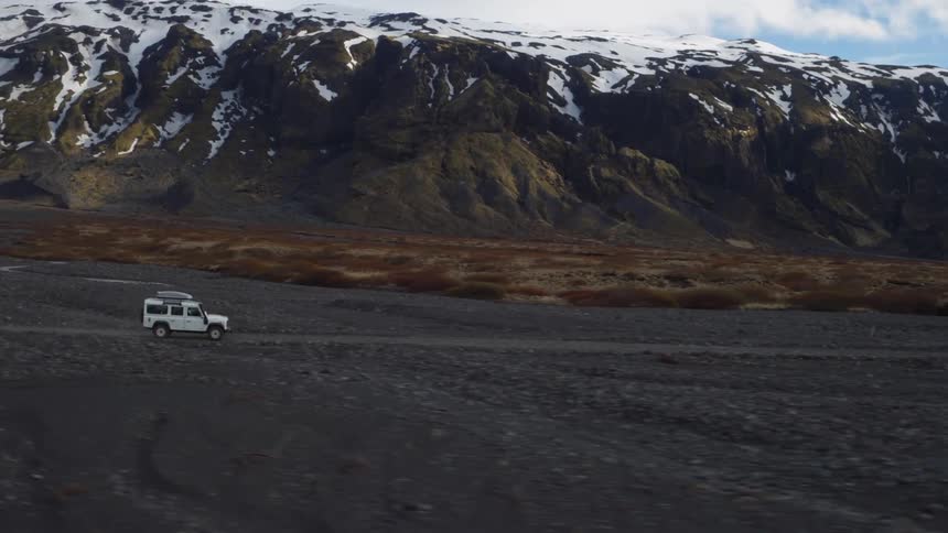 Aerial view of a vehicle driving a dirt trail snowy mountains in the background