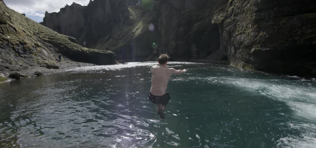 A shirtless man runs and jumps into a pond