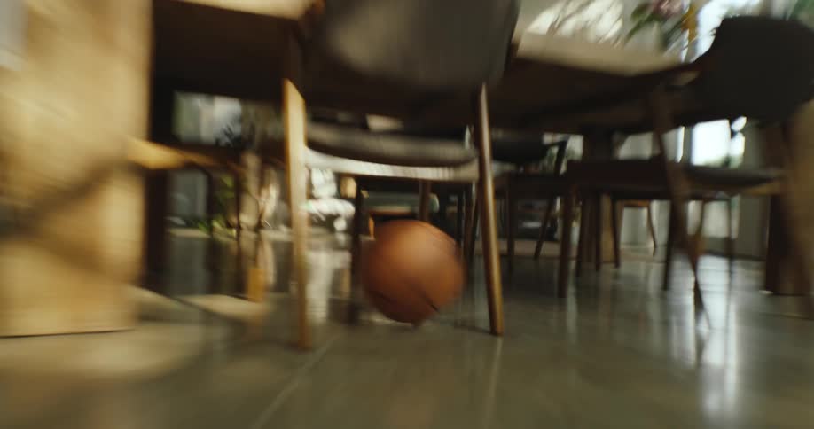 An orange basketball rolling in a kitchen going under the wooden table