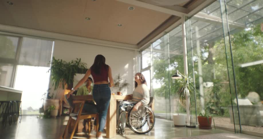Three women one of them in a wheelchair gather around a table to have tea