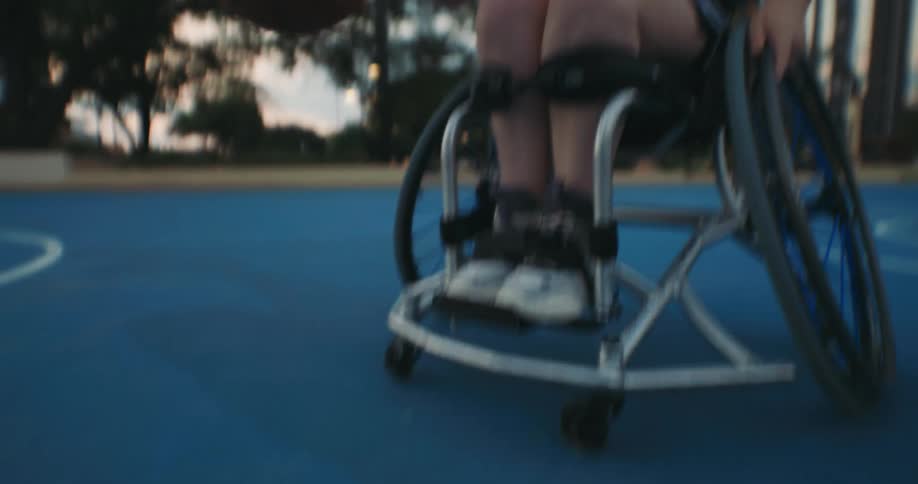 A young woman in a wheelchair playing basketball in a park dribbling the ball and spinning her chair