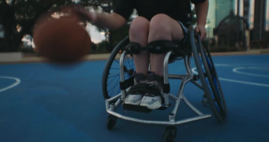 A person in a wheelchair dribbles a basketball before spinning away on a court in a city park