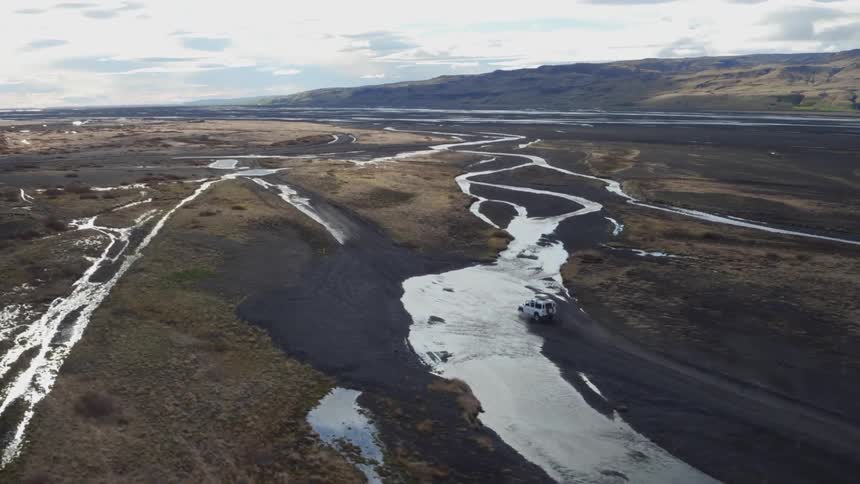 Aerial view of a vehicle driving through shallow water following a trail
