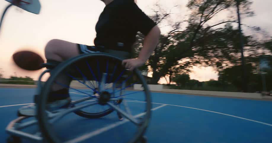A woman is in a wheelchair and playing basketball on a court with blue paint on the floor