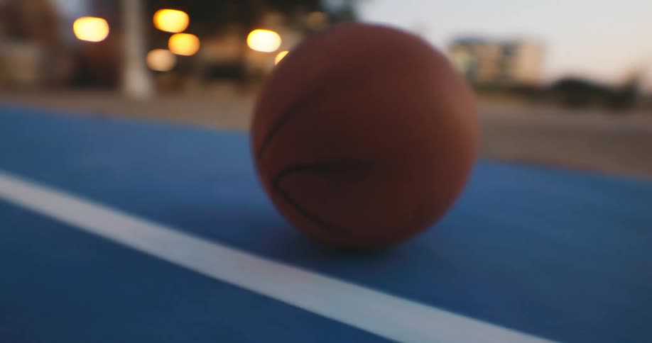 Basketball rolls across a basketball court after dusk