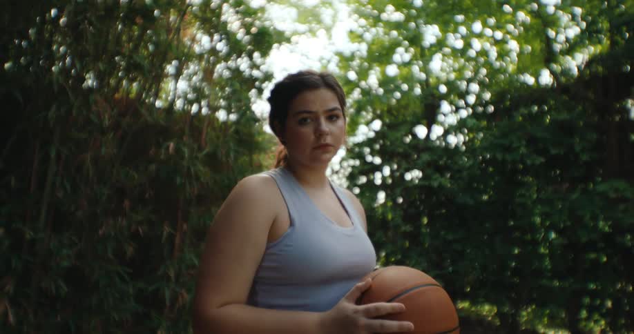 A teenage girl holds a basketball while sitting in a wheelchair in a garden