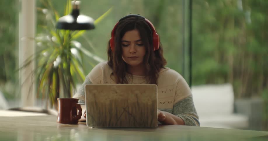 A young woman at a table on a laptop wearing red headphones