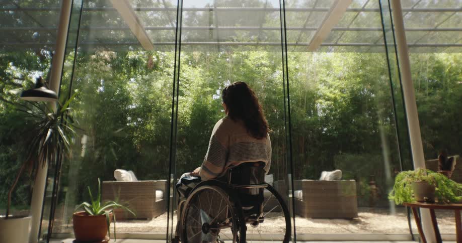 A woman sitting in a wheelchair in a large room in front of large glass windows