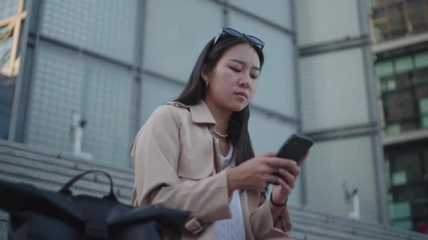 A young woman with glasses on her head is using her cell phone and she looks straight ahead and then looks back at her cell phone