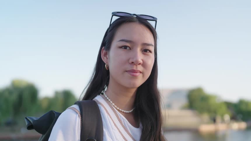 An asian woman smiles while standing near a river in a city