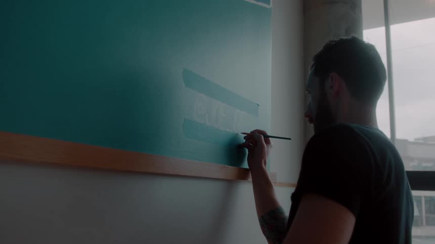 A man using a small brush and he is touching up green details of a green wall