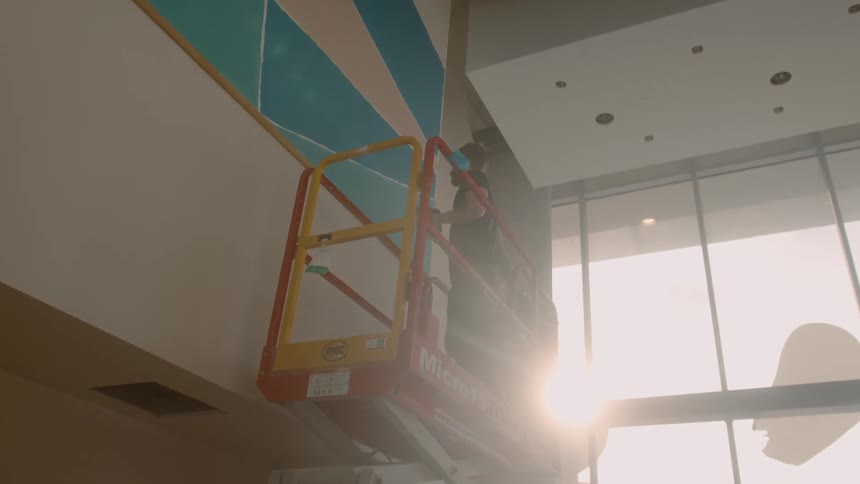A man on a lift paints uses a brush on the inside of a building