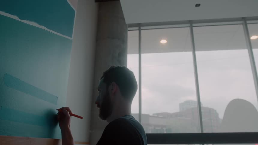 A man standing in front of a wall writing on a board as light shines through the large windows