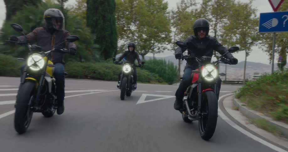 Three people ride motorcycles from a parking lot and into a tunnel