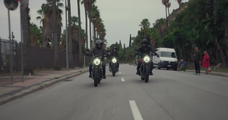 Three bikers with sports bikes and wearing black helmets driving on an asphalt street that has one lane blocked by cones