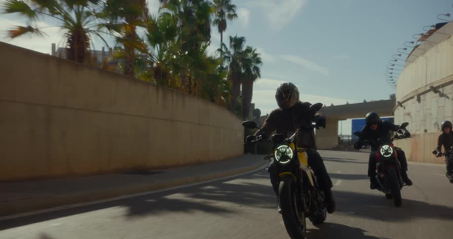Three motorcyclists ride their motorcycles along a city street and through a tunnel on a sunny day