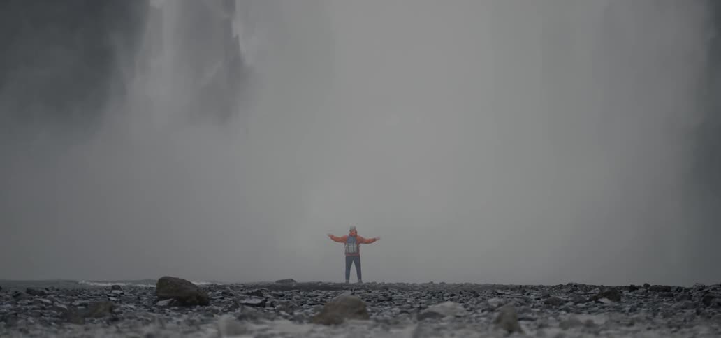 A person standing at the foot of a waterfall with their arms stretched out