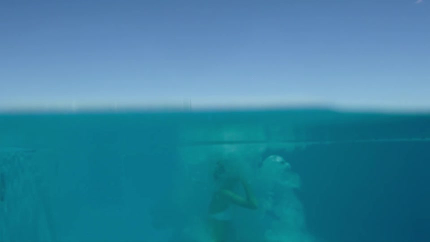 A woman runs and jumps into a pool of clear water and then she returns to the surface