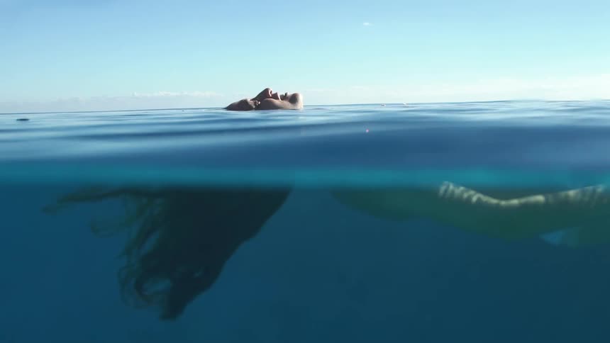 A woman is floating on the surface of the water and half of her body is submerged