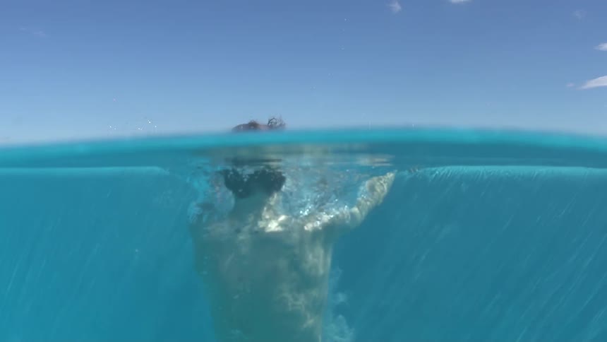 A man is on his back and entering a pool and sinking to the bottom
