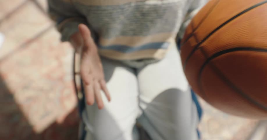 A young woman is sitting in a wheelchair and throwing a basketball from one hand to another