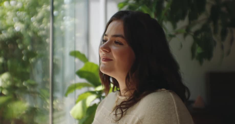 The face of a young woman who is giving a small smile and she is standing next to a glass window