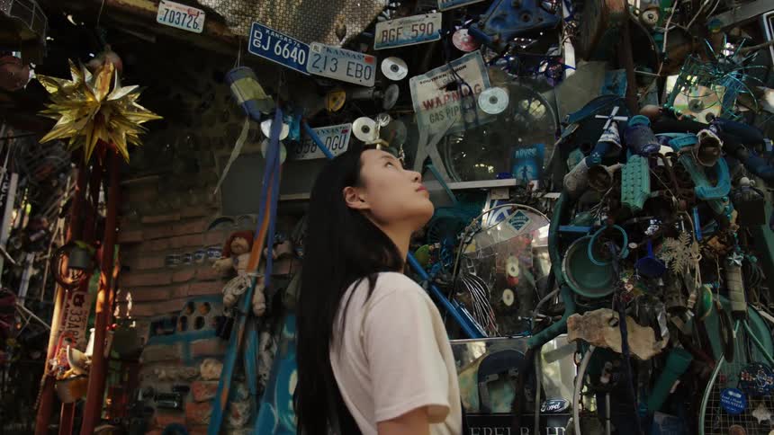 A woman is standing and looking at a wall covered in a sculpture made of random everyday items