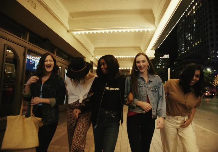 A group of happy friends walking side by side on a city sidewalk at night illuminated by overhead lights