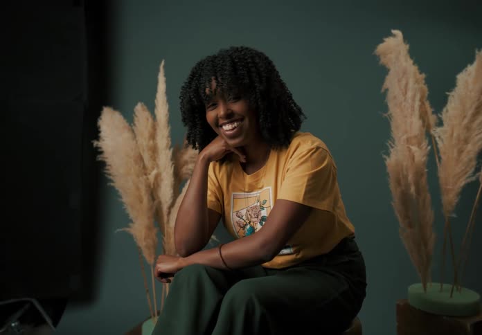 An young smiling woman sitting on a stool in a photography studio surrounded by large pampas grass arrangements