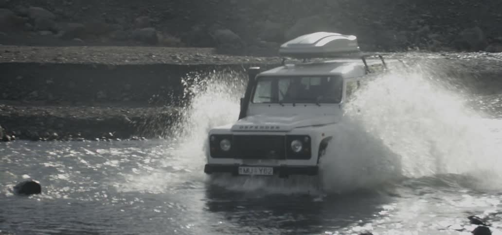 Suv crossing through some shallow water as it splashes high on each side of the vehicle