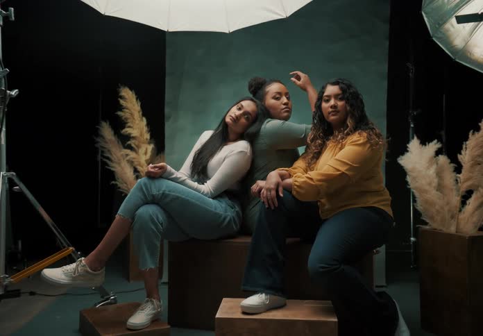 A photography studio setup with three young women posing surrounded by professional lighting equipment and decorative elements