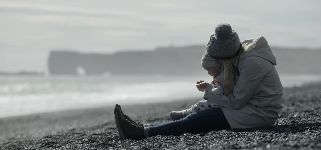 A woman and baby sit on a beach on a chilly day