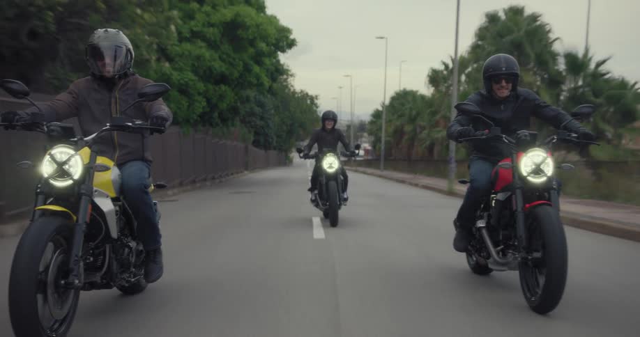 Three bikers wearing black clothes are riding on an asphalt street with colorful and sporty motorcycles