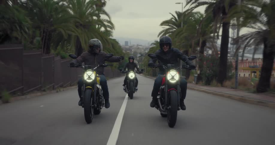 Three people ride motorcycles on a road outside of a city