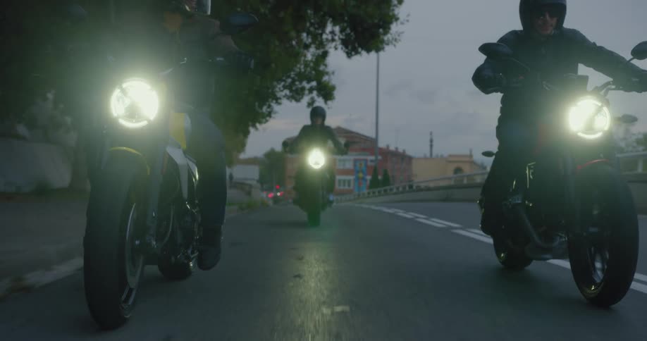 Three bikers riding a motorcycle on a lane of asphalt and they have their headlights on